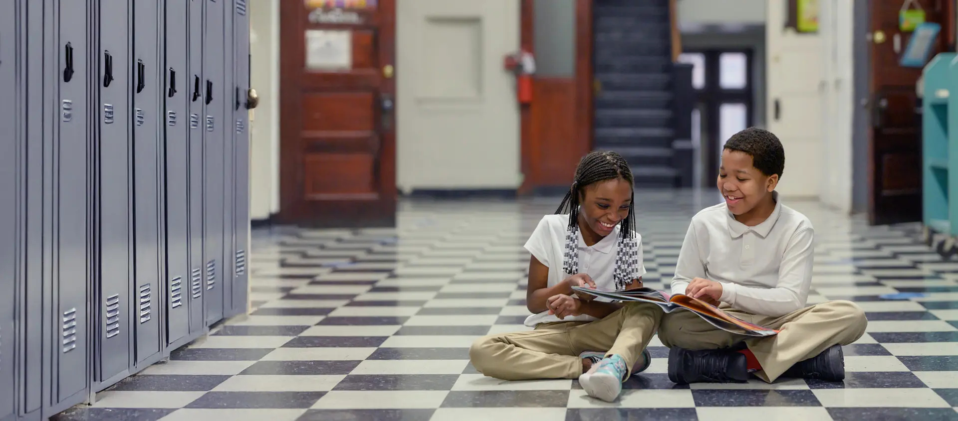 Two students sitting in school hallway looking at a book
